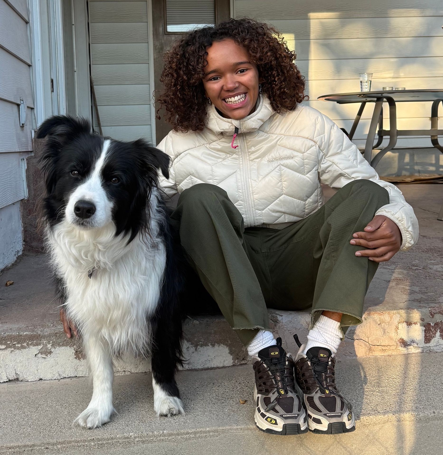 Person in a white jacket sitting on steps with a black and white dog.